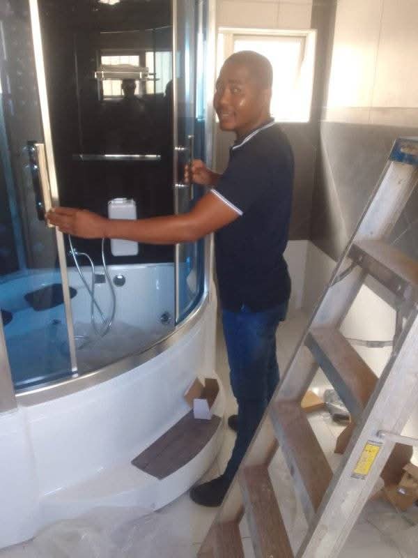 Plumber standing beside a curved glass shower enclosure on site
