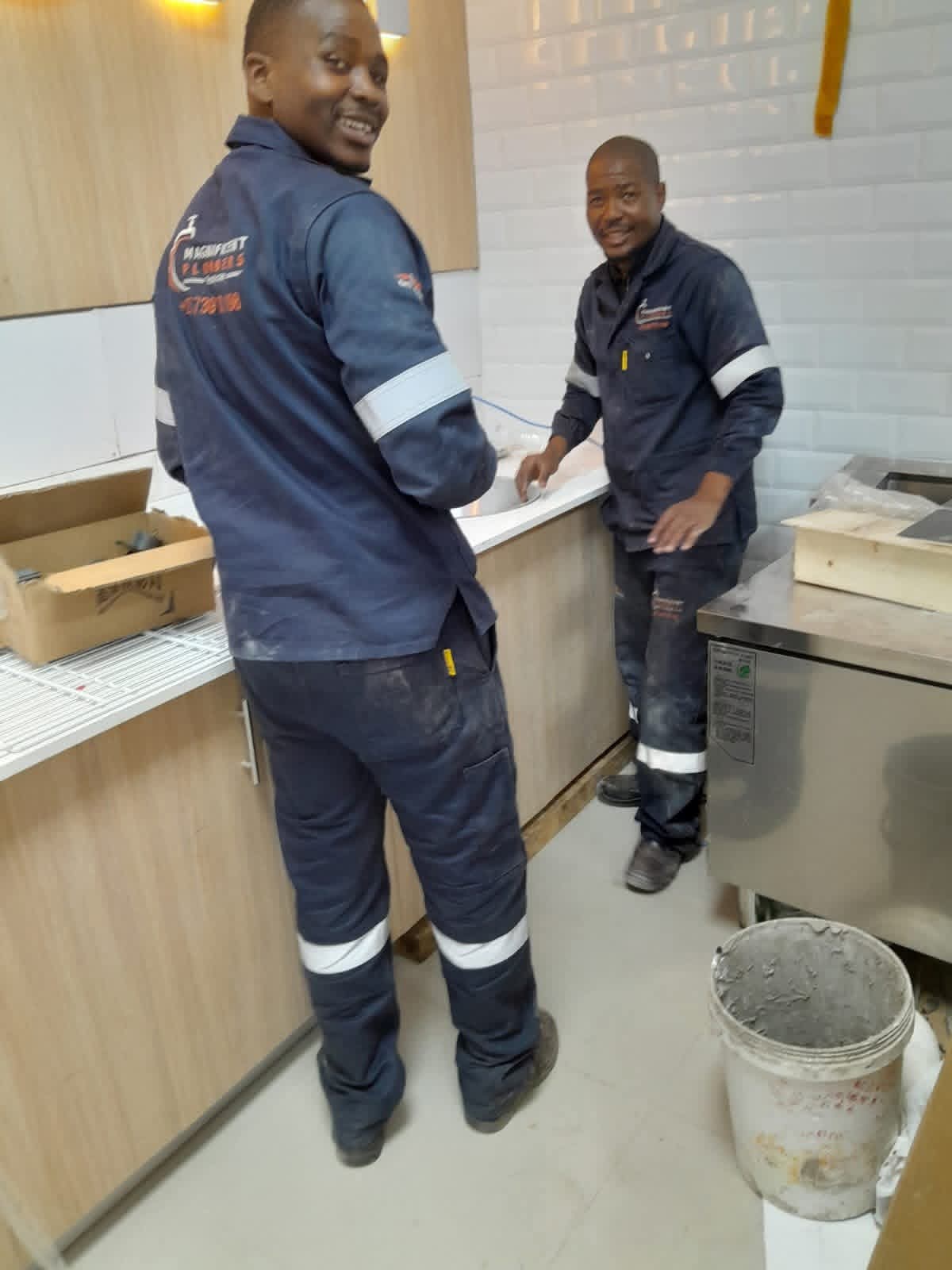 Two plumbers in branded uniforms working at a kitchen sink installation