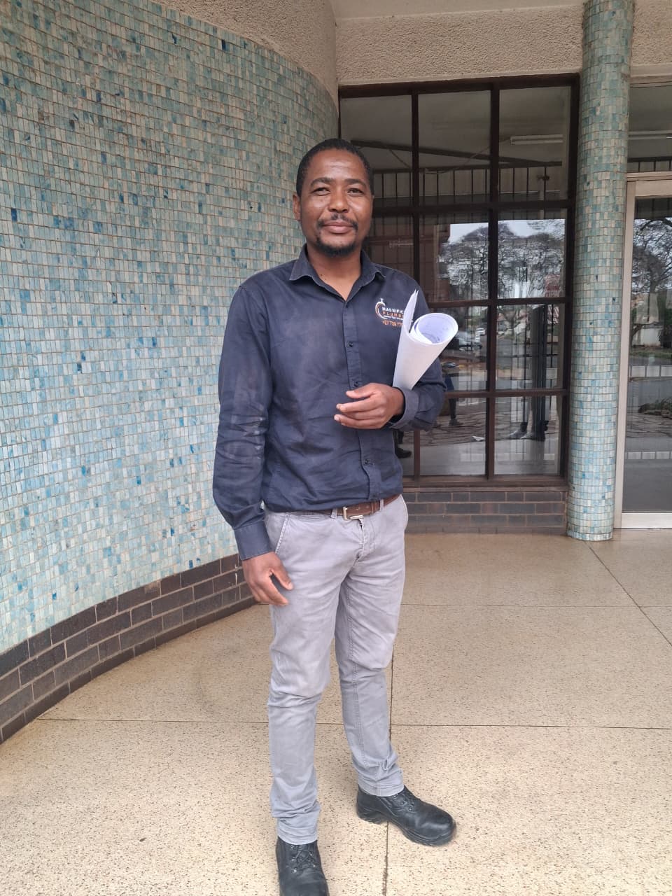 Contractor in branded uniform holding architectural blueprints outside a tiled building